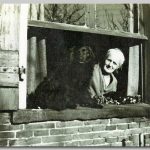 dame kijkend uit een raam met een zwarte hond