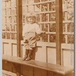 Gerard, 1915 Jongetje staand op een bank voor een muur van latwerk