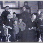 Gezin, 1917 Een hele ernstige familie zittend en staand in de hoek van een kamer. Klok, boeken en schilderijen op de achtergrond