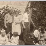 Gezin, 1930 Mensen staand en zittend in de tuin omringd door struiken