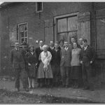 Gezin, 1930 Mensen in winterkleding staand voor een muur met ramen en bomen zonder bladeren