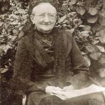 Oudere glimlachende dame , zwart gekleed met krant op haar schoot