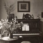 Huiskamer met piano en bosbloemen op een tafeltje