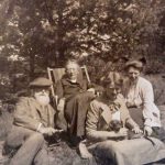 Fam Hundius, 1919 Vier mensen met een hond in een tuin met bomen