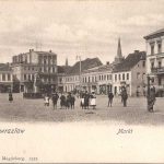 Markt met fontein in het midden, huizen er omheen en een paar lopende mensen