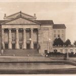 groot gebouw met zes zuilen en watervlakte er voor