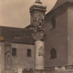 Een zuil met standbeeld er op voor een groot gebouw