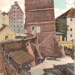 Scheve vierkante toren en groot gebouw met veel ramen op de achtergrond