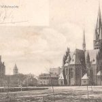 Kaal plein met kleine bompjes, grote kerk en hoge toren