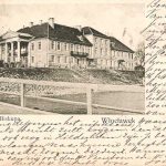 groot gebouw met aan een kant zuilen en hek er om heen